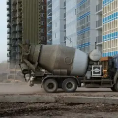 Betonomieszarka na placu budowy, w tle nowoczesne budynki. Kierowca betonomieszarki w pracy, dostarcza materiał.