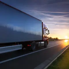 Kierowca zawodowy wyrusza w trasę o zachodzie słońca. Ciężarówka jedzie autostradą, a niebo jest pełne smug po samolotach.