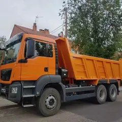 Pomarańczowa wywrotka na tle drzew i domu. Czy można mieć kat C bez B? Tak, to możliwe, jeśli masz odpowiednie szkolenie.