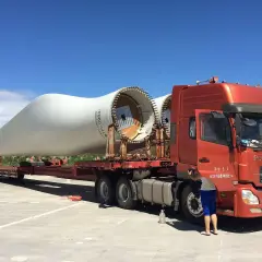 Ciężarówka transportuje łopatę turbiny wiatrowej. To ważny element w kraju tranzytowym, czekający na dalszą podróż.
