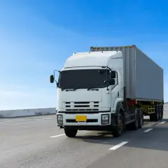 Biały tir z kontenerem jedzie autostradą. Wzór umowy zlecenie dla kierowcy tira jest dostępny online.