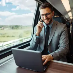 Biznesmen w garniturze rozmawia przez telefon i pracuje na laptopie w pociągu. Planuje swoją dietę zagraniczną w Niemczech.