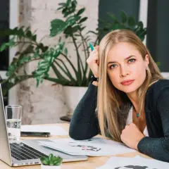 Blondynka z zielonym długopisem w dłoni, zastanawia się nad różnymi rodzajami odpoczynku, siedząc przy biurku z laptopem.
