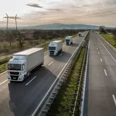 Ciężarówki jadące autostradą, zjazd na bazę pakiet mobilności. W tle góry i linie energetyczne.