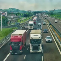 Kierowca zawodowy w trasie, ciężarówki na autostradzie. W tle znak Esso i zielone wzgórza.