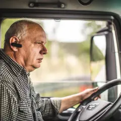 Kierowca ciężarówki w słuchawce Bluetooth, skupiony na drodze. Przestrzega rozporządzenie 561 czas pracy kierowców, dbając o bezpieczeństwo.