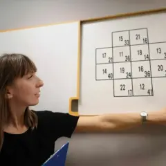 Kobieta przy tablicy z zadaniem matematycznym, które może być częścią testów psychologicznych. Zastanawia się, ile trwają psychotesty.
