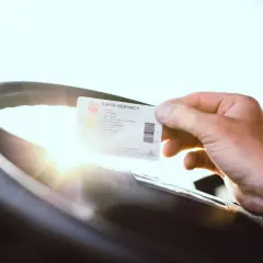 Dłoń trzyma kartę kierowcy przy kierownicy. To ważny dokument dla każdego, kto planuje kurs na przewóz rzeczy.