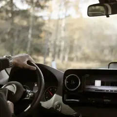 Mężczyzna za kierownicą, zegarek na ręku, widok na drogę i las. Czyżby to było przekroczenie czasu jazdy?