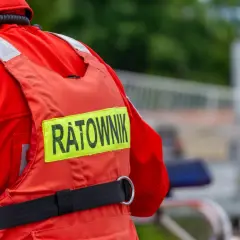 Ratownik w czerwonym stroju, z napisem "RATOWNIK" na kamizelce. Może to być sytuacja, gdy ktoś próbuje kierować ruchem bez uprawnień, a ratownik jest na miejscu.
