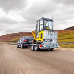 Czarny SUV ciągnie na lawecie minikoparkę JCB. Czy na lawetę trzeba mieć uprawnienia?