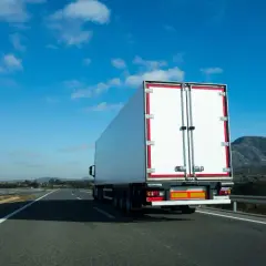 Biała naczepa ciężarówki na autostradzie, przewożąca fracht. Co to jest fracht? To towar w transporcie.