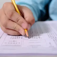 Dłoń z ołówkiem wypełniająca arkusz testowy z okienkami wyboru.