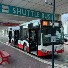 Autobus wahadłowy czeka na pasażerów pod znakiem "SHUTTLE BUS". Drzwi otwarte, gotowy do przewozu.