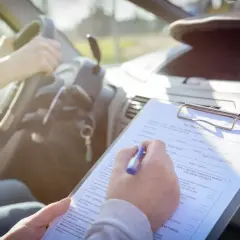 Osoba siedząca za kierownicą samochodu wypełnia dokumentację dotyczącą badań psychologicznych na prawo jazdy.
