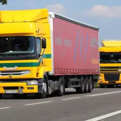 Dwa żółte ciężarówki jadące drogą. Kierowcy wykonujący przewozy drogowe powinni wiedzieć, ile godzin trwa szkolenie okresowe.