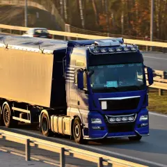 Niebieska ciężarówka z naczepą jedzie autostradą. Kierowca z kodem 95 prawo jazdy wiezie towar.