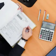 Osoba w garniturze przegląda dokumenty, obok kalkulator i długopisy. To praca doradcy ADR.