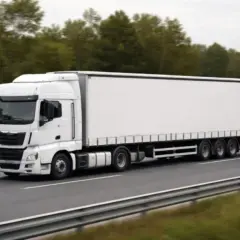 Biała ciężarówka z naczepą jedzie po drodze. Jej dopuszczalna masa całkowita tira jest znacząca, co widać po liczbie osi.