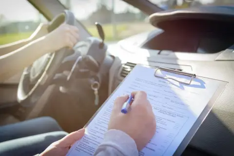 Osoba siedząca za kierownicą samochodu wypełnia dokumentację dotyczącą badań psychologicznych na prawo jazdy.