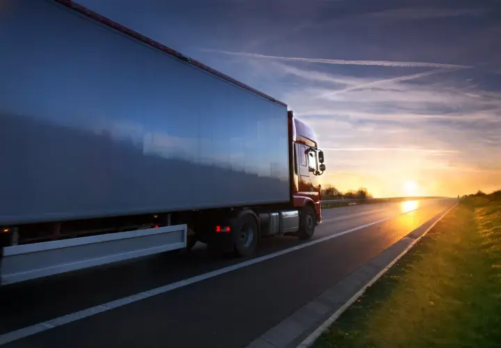 Kierowca zawodowy wyrusza w trasę o zachodzie słońca. Ciężarówka jedzie autostradą, a niebo jest pełne smug po samolotach.