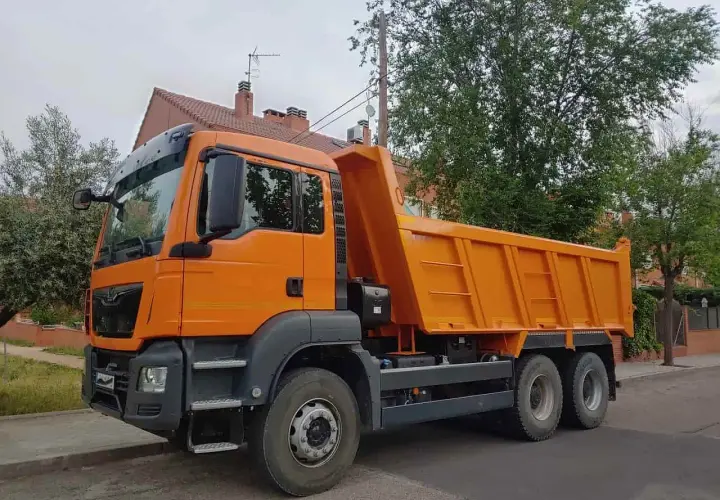 Pomarańczowa wywrotka na tle drzew i domu. Czy można mieć kat C bez B? Tak, to możliwe, jeśli masz odpowiednie szkolenie.