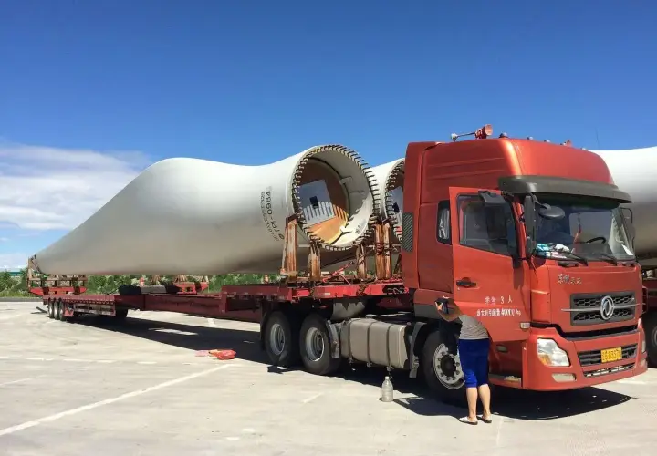 Ciężarówka transportuje łopatę turbiny wiatrowej. To ważny element w kraju tranzytowym, czekający na dalszą podróż.