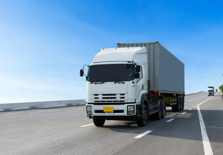 Biały tir z kontenerem jedzie autostradą. Wzór umowy zlecenie dla kierowcy tira jest dostępny online.