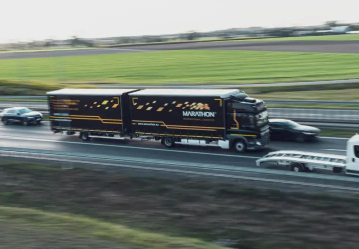 Ciężarówka Marathon International Logistics na autostradzie, obok samochód osobowy i laweta. To transport bilateralny przykład.