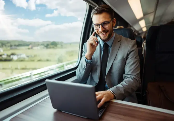Biznesmen w garniturze rozmawia przez telefon i pracuje na laptopie w pociągu. Planuje swoją dietę zagraniczną w Niemczech.