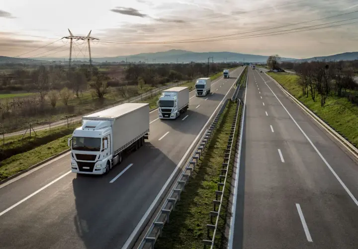 Ciężarówki jadące autostradą, zjazd na bazę pakiet mobilności. W tle góry i linie energetyczne.