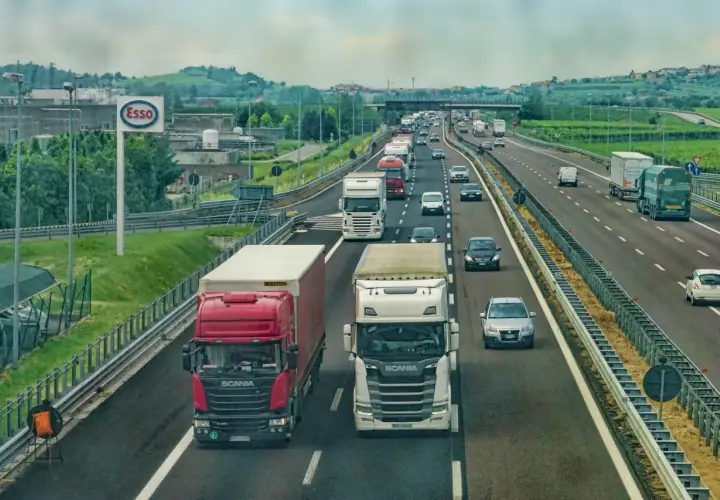 Kierowca zawodowy w trasie, ciężarówki na autostradzie. W tle znak Esso i zielone wzgórza.