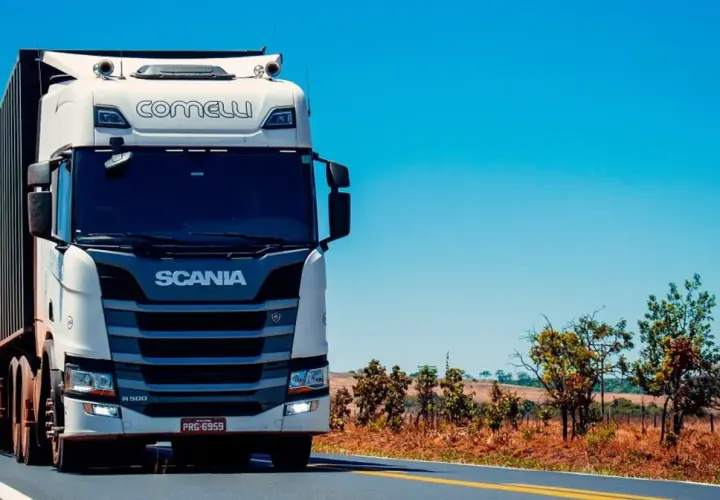 Biała ciężarówka Scania z naczepą jedzie po pustej drodze, zapowiadając zasłużoną pauzę weekendową.