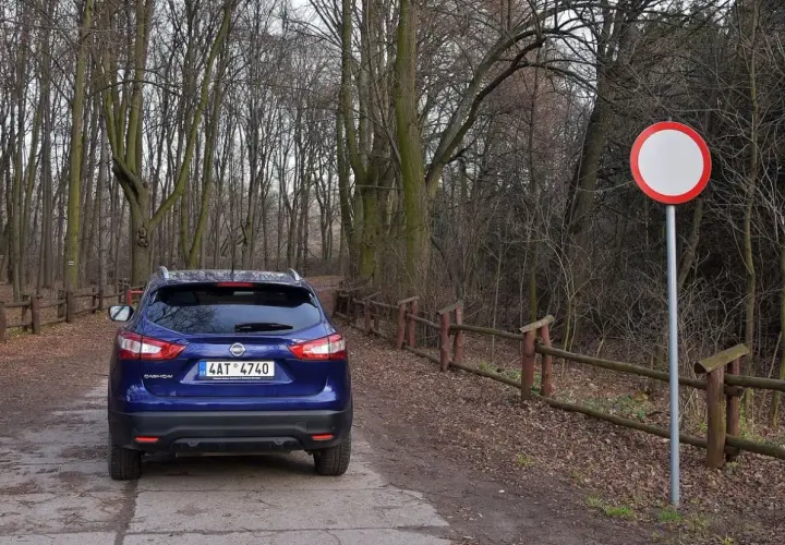 Niebieski Nissan na leśnej drodze, obok znak zakazu ruchu. Kierowca ryzykował wjazd pod zakaz ruchu, mandat murowany.