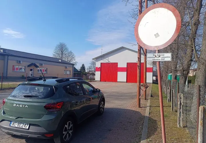 Znak zakazu wjazdu i samochód Dacia przed remizą OSP. Czy wjazd pod zakaz tonażowy grozi mandatem i punktami?
