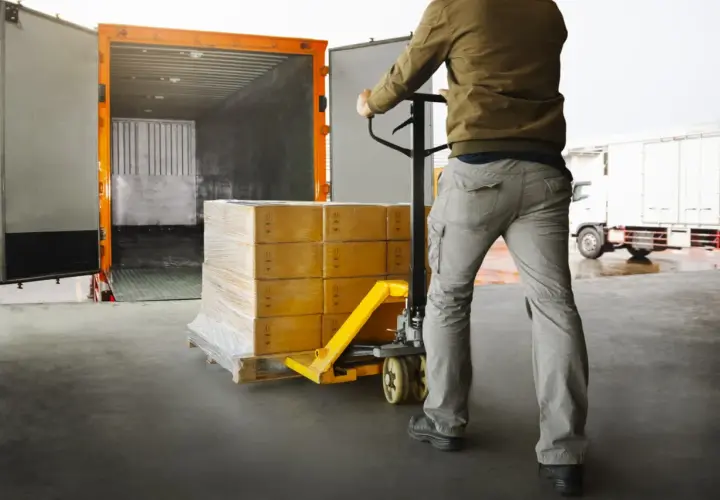 Pracownik magazynu przemieszcza paletę z paczkami za pomocą wózka widłowego, przygotowując towar do **cross trade** transportu.