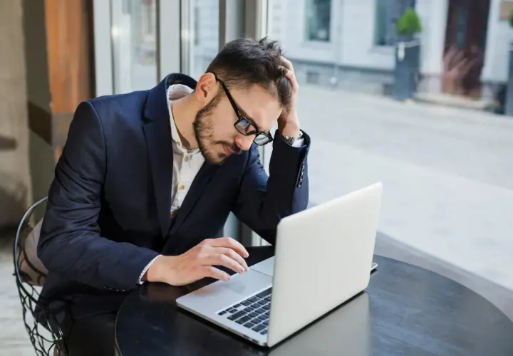 Zestresowany mężczyzna w garniturze pracuje przy laptopie, próbując skrócenie pauzy do 7 godzin.