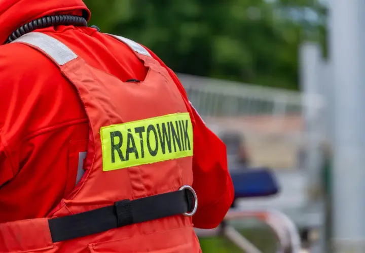 Ratownik w czerwonym stroju, z napisem "RATOWNIK" na kamizelce. Może to być sytuacja, gdy ktoś próbuje kierować ruchem bez uprawnień, a ratownik jest na miejscu.