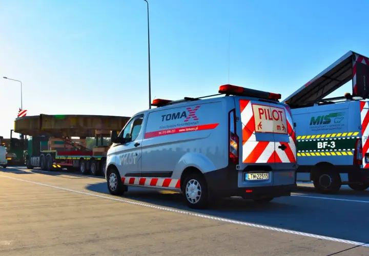 Pojazd ponadgabarytowy transportowany na platformie, eskortowany przez dwa samochody pilotujące z napisem "PILOT".