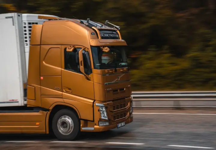 Złoty ciągnik siodłowy z naczepą jedzie drogą. Prawo przewozowe reguluje takie transporty, zapewniając bezpieczeństwo i płynność ruchu.