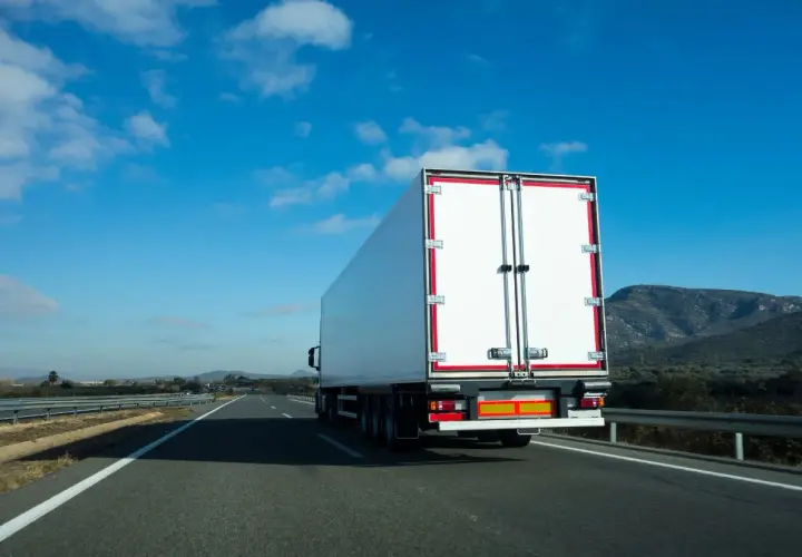 Biała naczepa ciężarówki na autostradzie, przewożąca fracht. Co to jest fracht? To towar w transporcie.