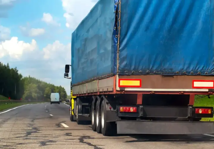Ciężarówka z niebieską plandeką jedzie drogą. Kierowca uważa na zakaz jazdy na Węgrzech, by uniknąć kary.