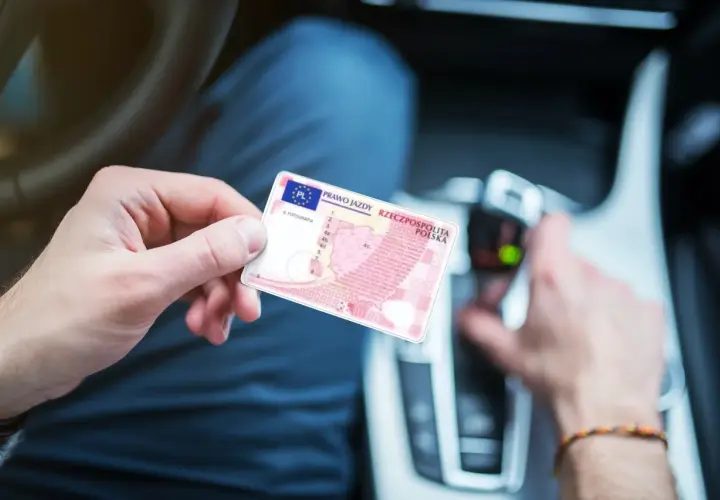Osoba trzyma polskie prawo jazdy. W tle widać wnętrze samochodu, co sugeruje, że może to być dokument potrzebny do prowadzenia pojazdu, gdy posiada się prawo jazdy spoza Unii Europejskiej.