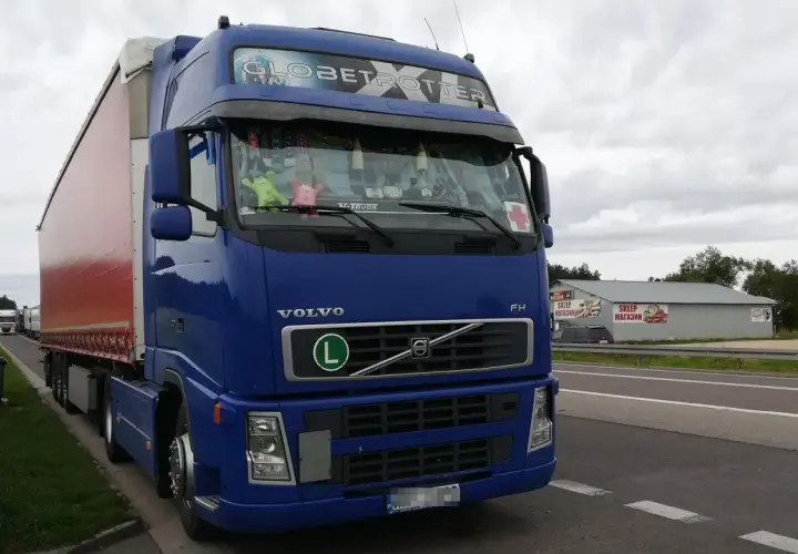Niebieski Volvo FH Globetrotter z naczepą, zaparkowany przy drodze. W tle sklep i inne ciężarówki. Zakazy dla ciężarówek 40ton.