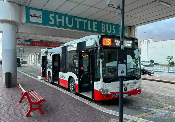 Autobus wahadłowy czeka na pasażerów pod znakiem "SHUTTLE BUS". Drzwi otwarte, gotowy do przewozu.