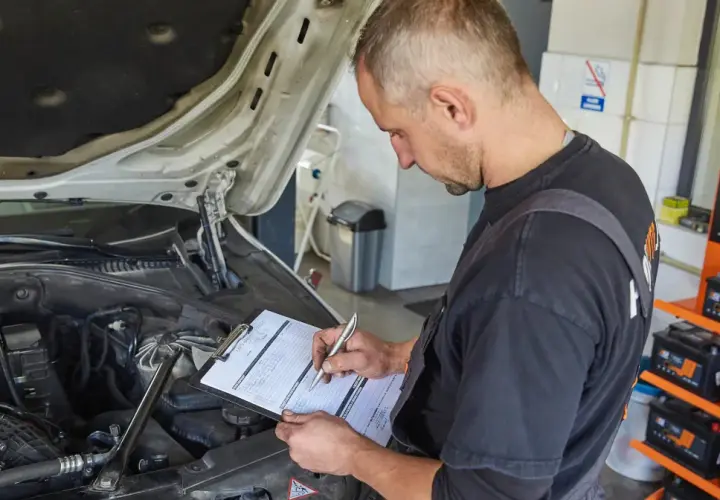 Mechanik spisuje stan techniczny pojazdu na karcie naprawy. W tle widać akumulatory.
