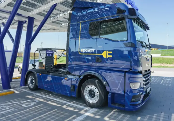 Niebieska ciężarówka elektryczna MAN eTGX z logo "epower" ładuje się pod panelem słonecznym. To przyszłość transportu, zgodna z normą euro 7.