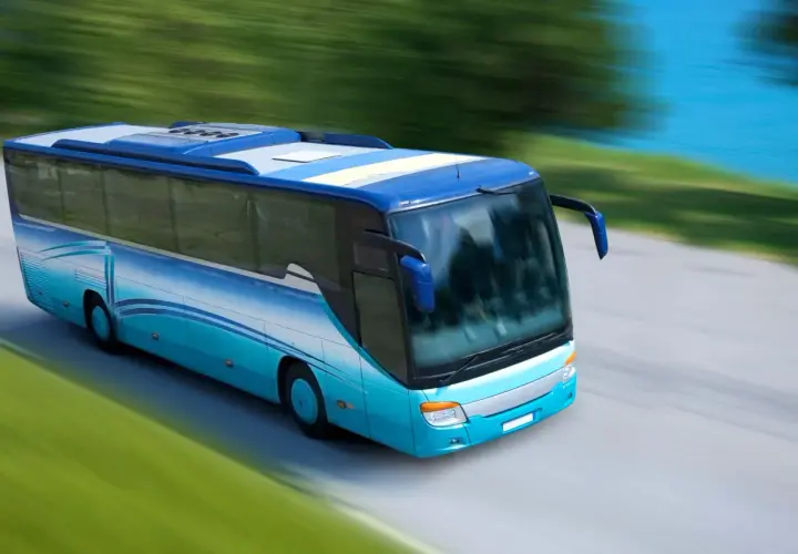 Niebieski autokar z licencją na międzynarodowy przewóz osób do 9 osób pędzi wzdłuż malowniczej trasy nad wodą.