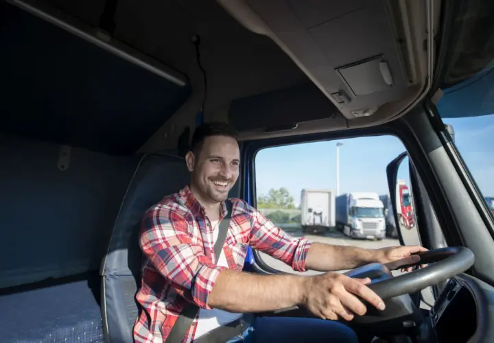 Uśmiechnięty kierowca w kratę za kierownicą ciężarówki. To jego dzień transportowca, gotowy na kolejną trasę.