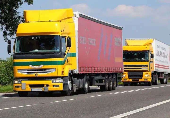 Dwa żółte ciężarówki jadące drogą. Kierowcy wykonujący przewozy drogowe powinni wiedzieć, ile godzin trwa szkolenie okresowe.